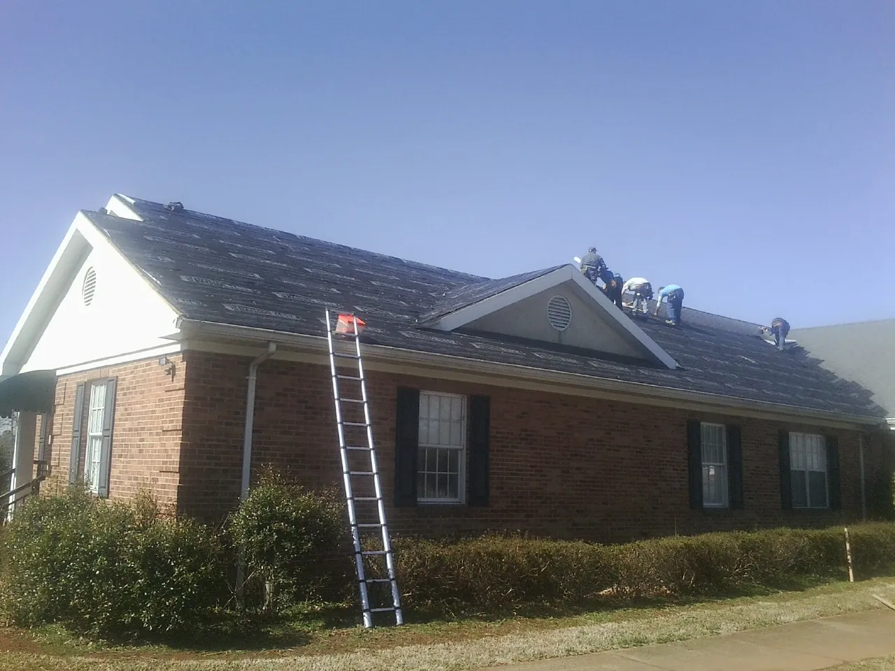 Crew tearing shingles off a brick ranch roof with a ladder set — Emergency Roof Repair work by our crew in Fairplay